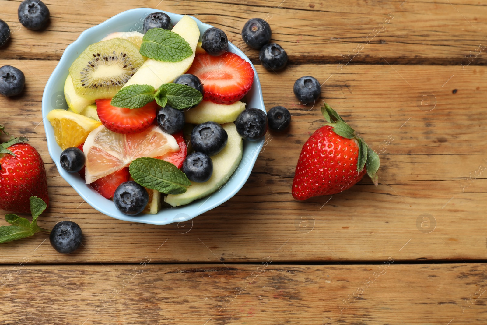 Photo of Tasty fruit salad in bowl and ingredients on wooden table, flat lay