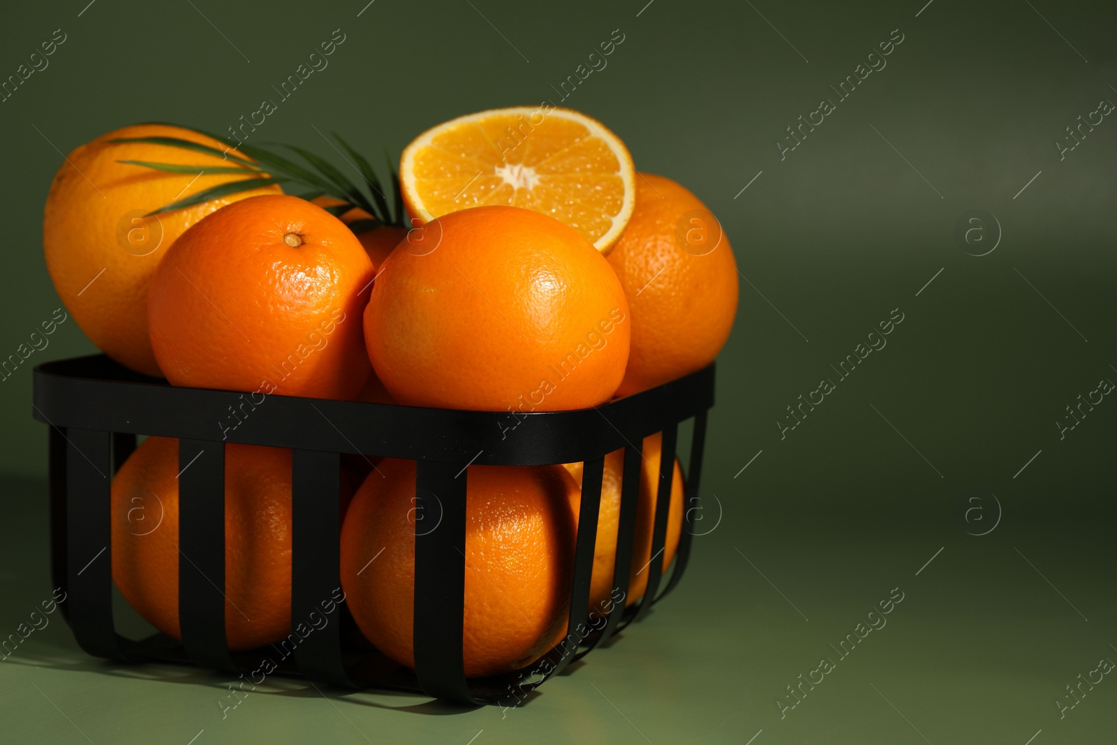 Photo of Fresh oranges in metal basket on green background, closeup. Space for text