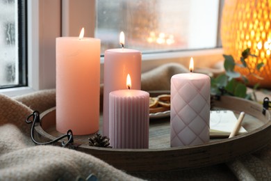 Photo of Tray with burning wax candles and decor on window sill indoors