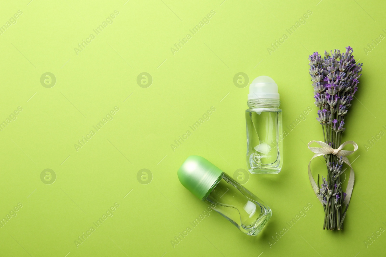 Photo of Female deodorants and lavender flowers on green background, flat lay. Space for text