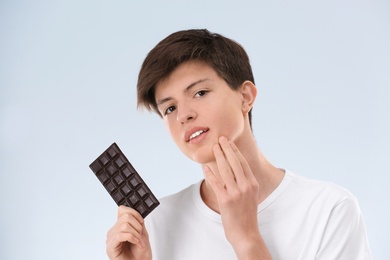Photo of Teenage boy with acne problem holding chocolate on light background. Skin allergy
