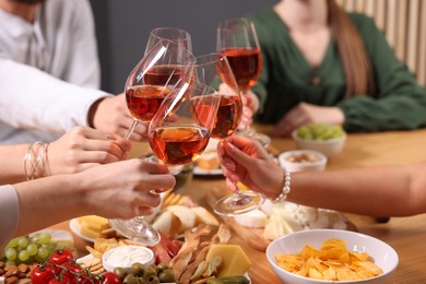 People clinking glasses with rose wine above wooden table, closeup