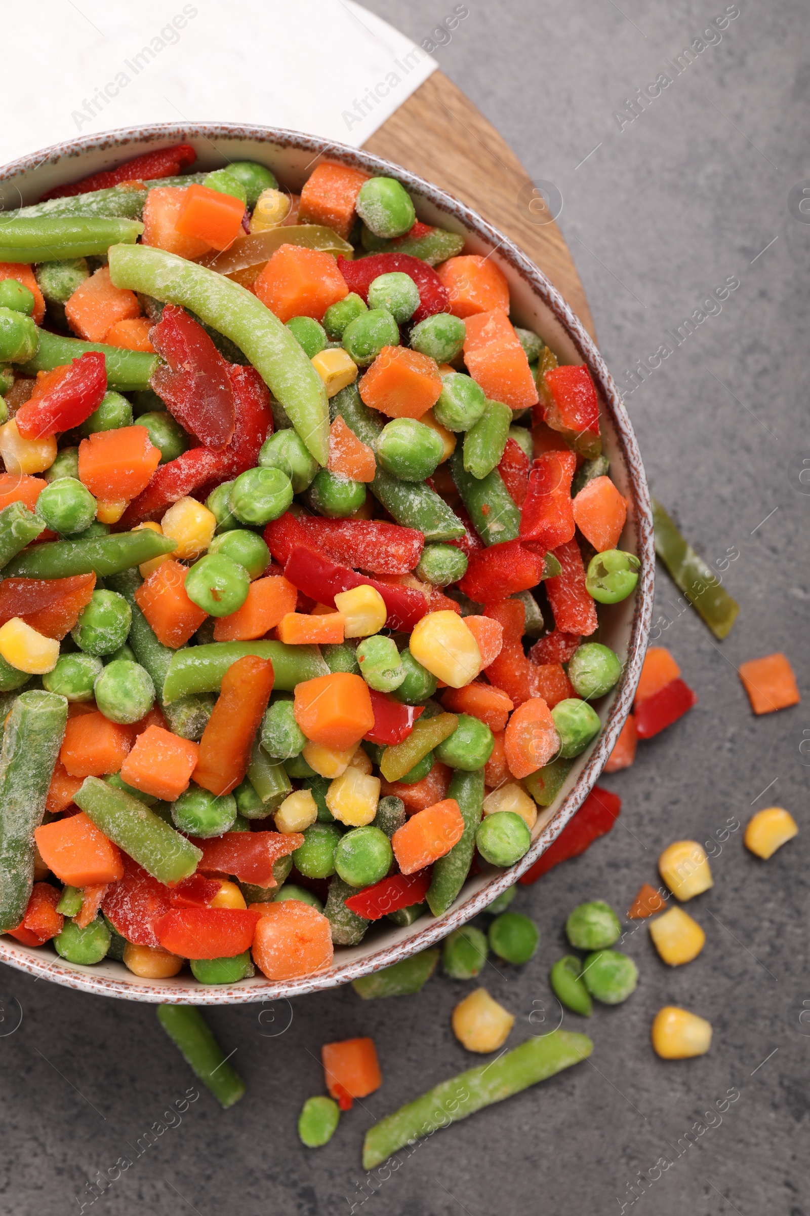 Photo of Mix of different frozen vegetables in bowl on grey table, top view