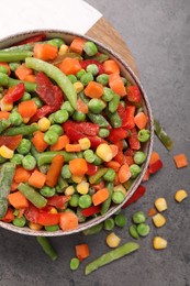 Mix of different frozen vegetables in bowl on grey table, top view