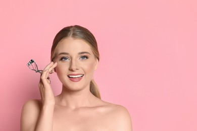 Photo of Young woman with eyelash curler on pink background, space for text