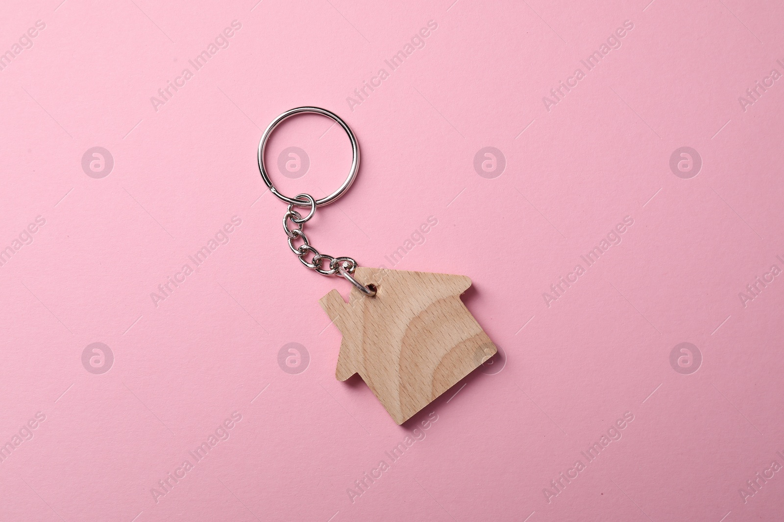 Photo of Wooden keychain in shape of house on pink background, top view