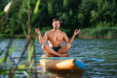 Photo of Man meditating on color SUP board on river