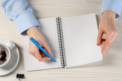 Photo of Woman writing in notebook at white wooden table, top view