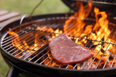 Photo of Tasty meat on barbecue grill with fire flames outdoors, closeup