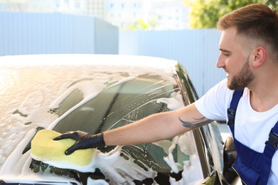 Young worker cleaning automobile with sponge at car wash