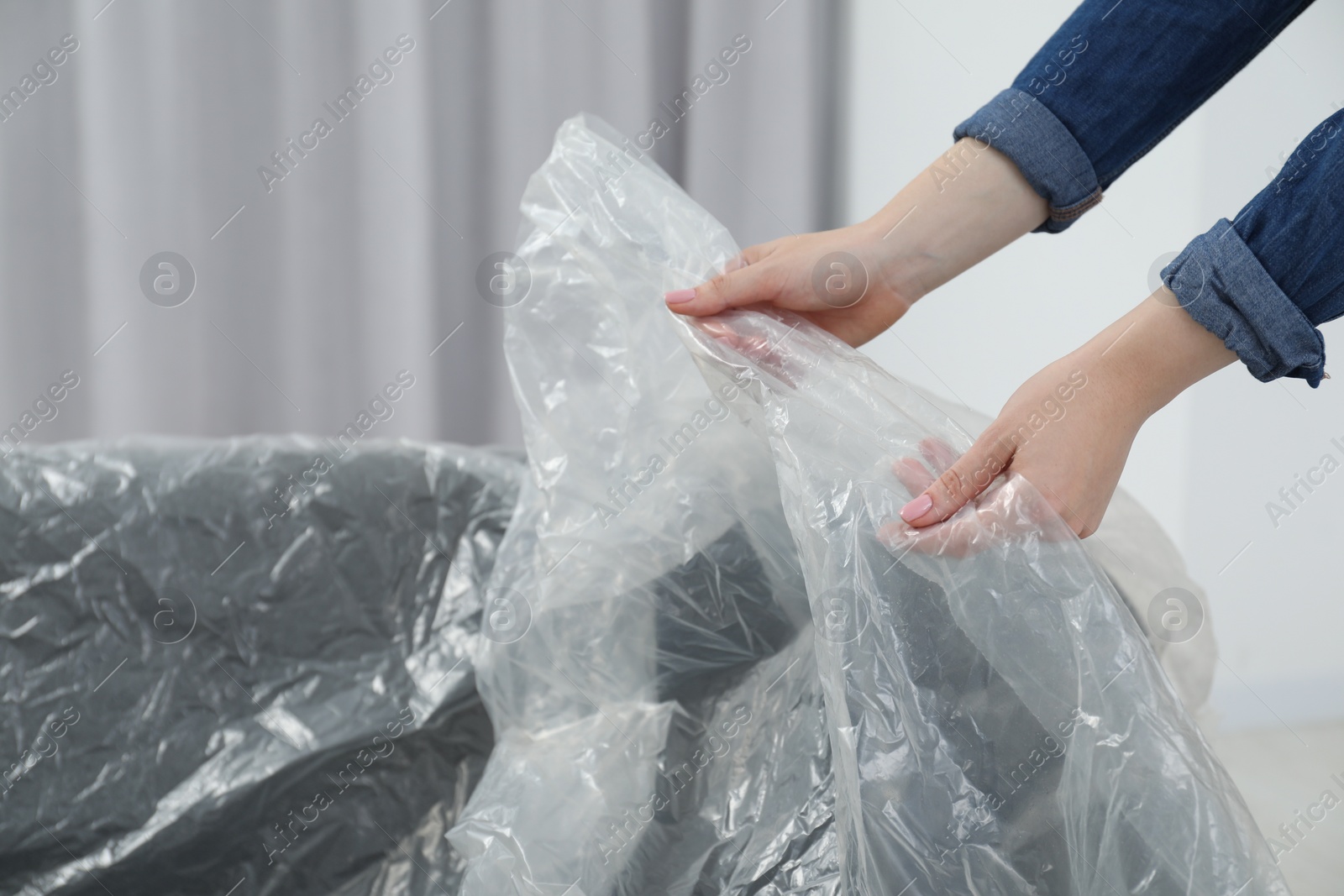 Photo of Woman putting plastic film away from sofa at home, closeup