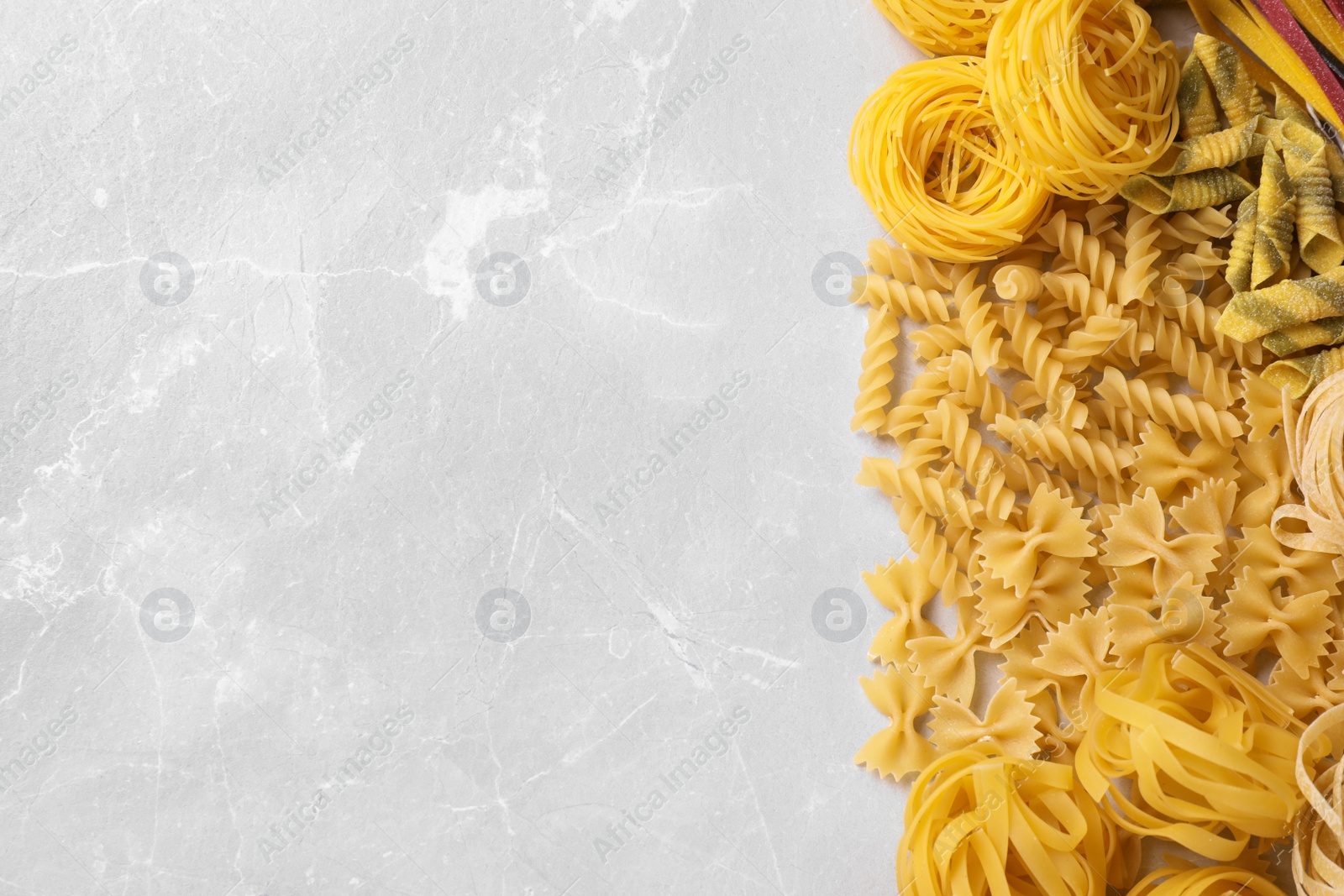 Photo of Different types of pasta on light grey marble table, flat lay. Space for text