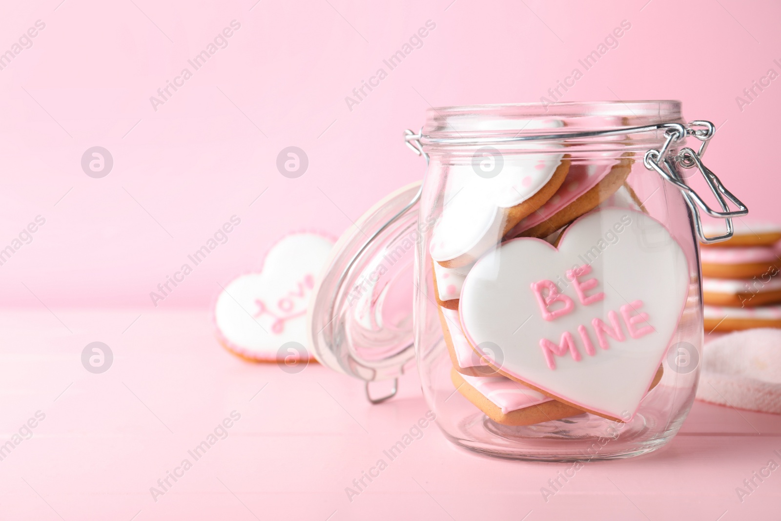 Photo of Heart shaped cookies in glass jar on pink background, space for text. Valentine's day treat
