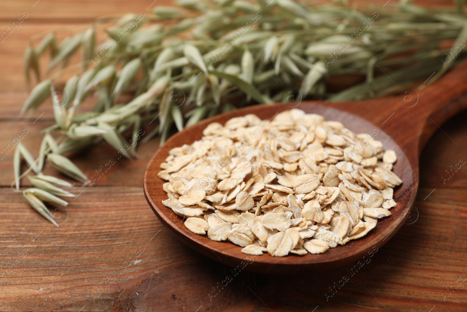 Photo of Spoon with oatmeal and floret branches on wooden table, closeup