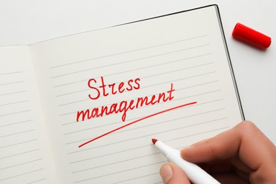 Man writing words Stress Management in notebook on white background, top view