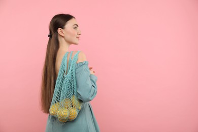 Woman with string bag of fresh lemons on pink background, space for text