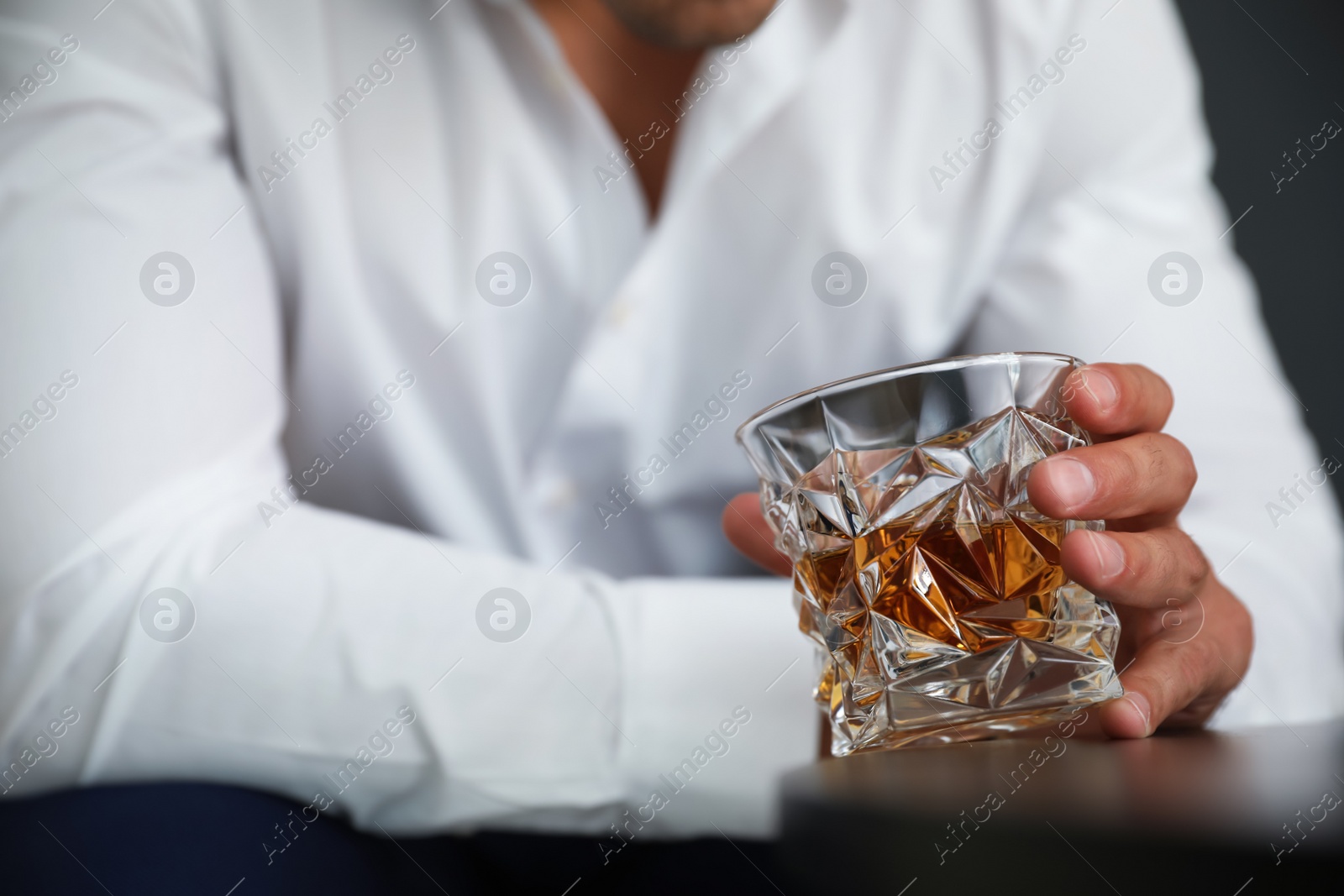 Photo of Young man with glass of whiskey at table, closeup view. Space for text
