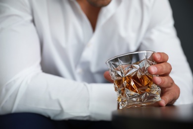 Young man with glass of whiskey at table, closeup view. Space for text