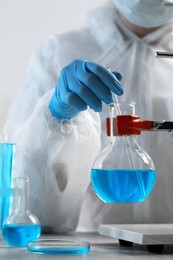 Photo of Scientist taking sample of light blue liquid in laboratory, closeup