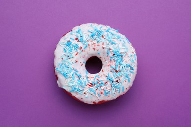 Photo of Sweet glazed donut decorated with sprinkles on purple background, top view. Tasty confectionery