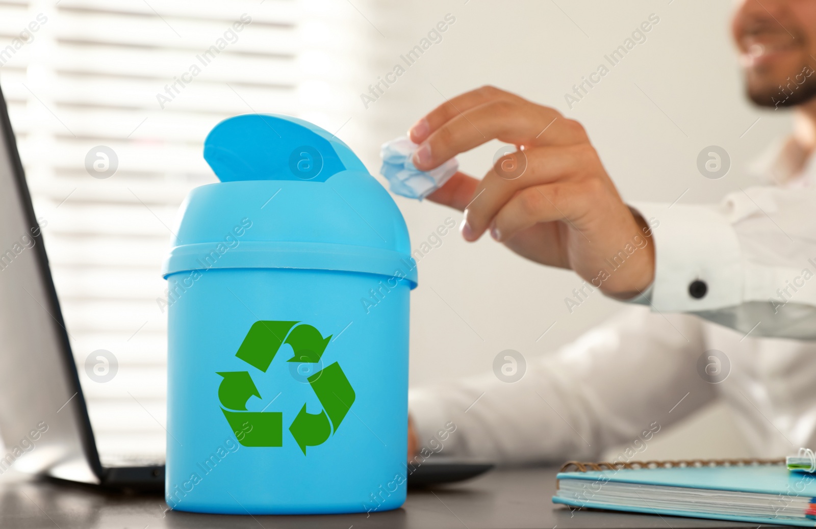 Photo of Young man throwing paper into mini recycling bin at table in office, closeup