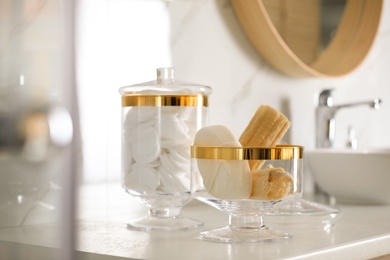 Photo of Jars with cotton pads and loofah sponges on countertop in bathroom