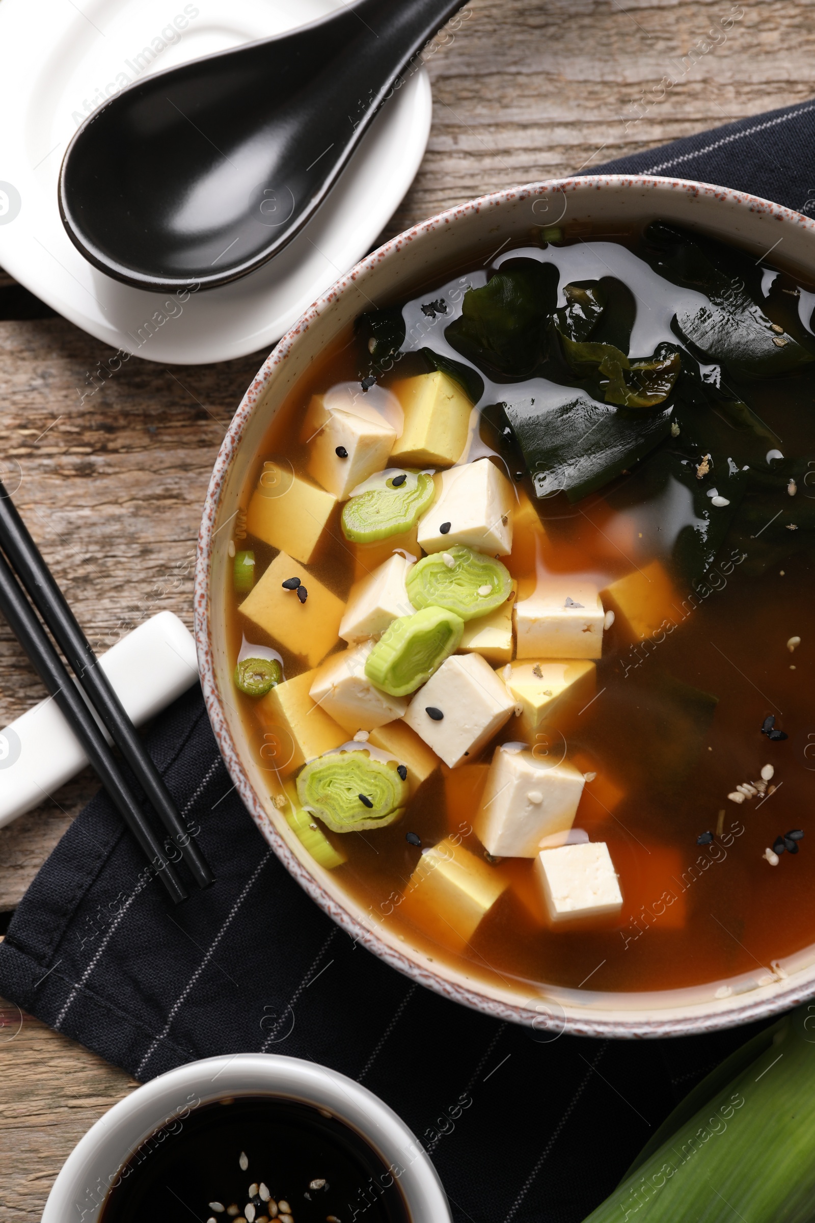 Photo of Bowl of delicious miso soup with tofu served on wooden table, flat lay
