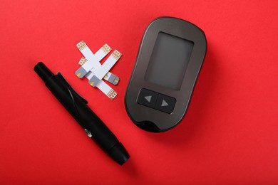 Photo of Digital glucometer, lancet pen and test strips on red background, flat lay with space for text. Diabetes control