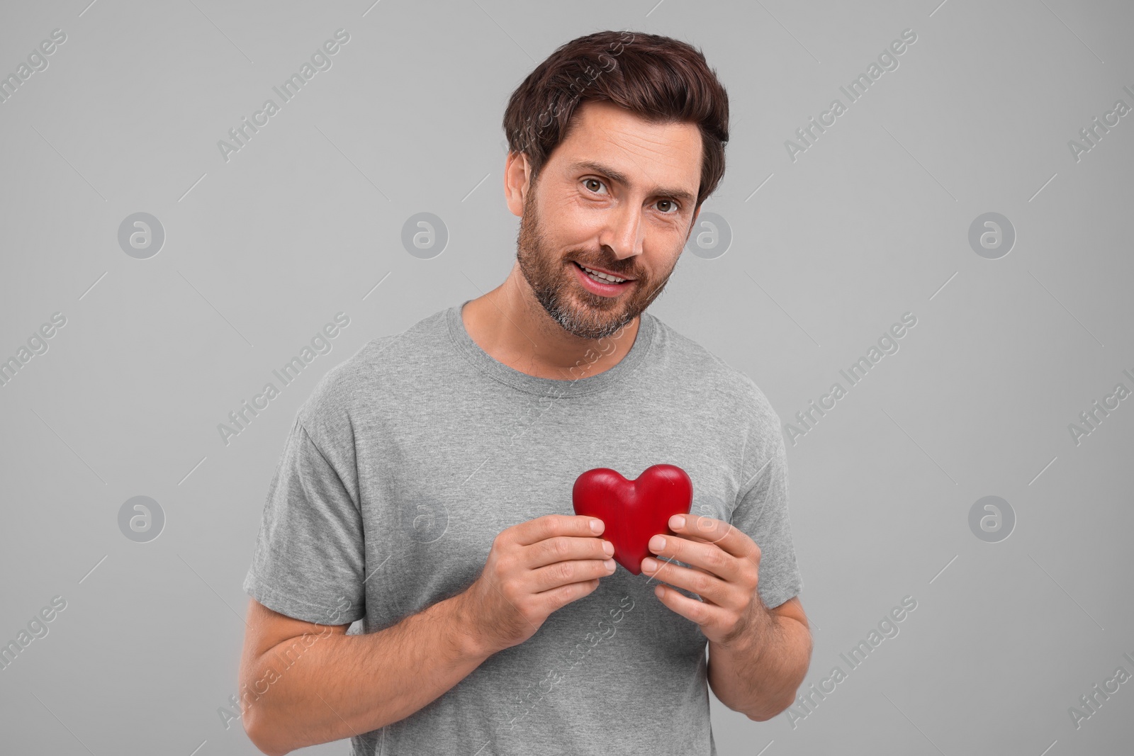 Photo of Happy man holding red heart on grey background