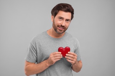 Happy man holding red heart on grey background