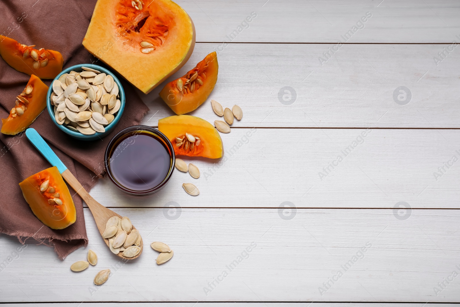 Photo of Flat lay composition with glass bowl of pumpkin seed oil on white wooden table. Space for text