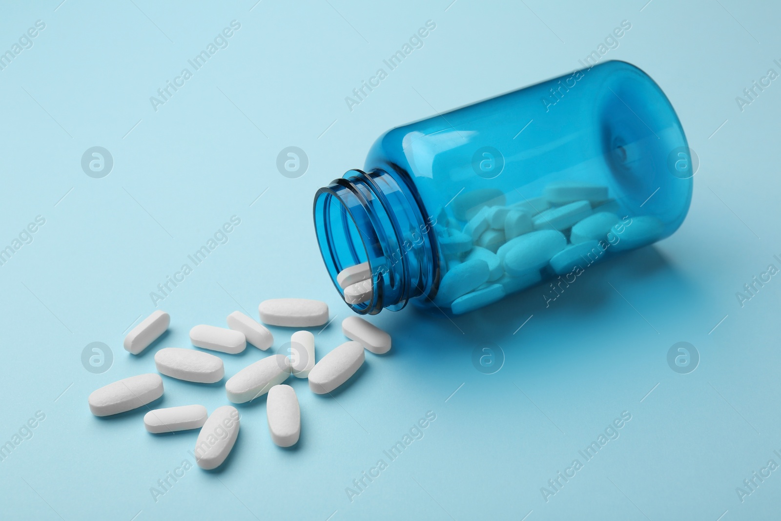 Photo of Vitamin pills and bottle on light blue background, closeup