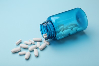 Photo of Vitamin pills and bottle on light blue background, closeup