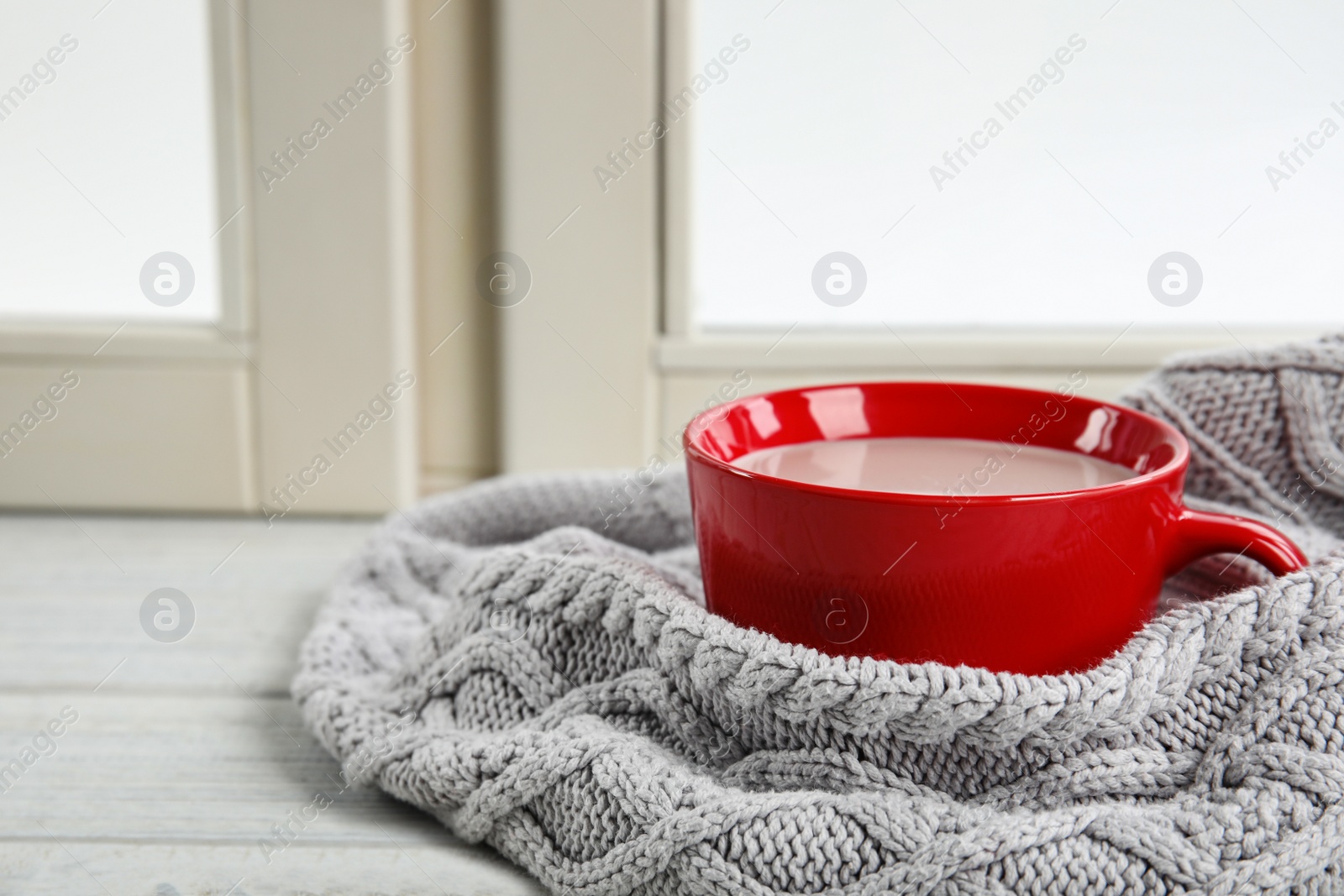 Photo of Cup of hot cocoa and knitted sweater on window sill. Winter drink