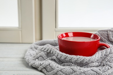 Photo of Cup of hot cocoa and knitted sweater on window sill. Winter drink