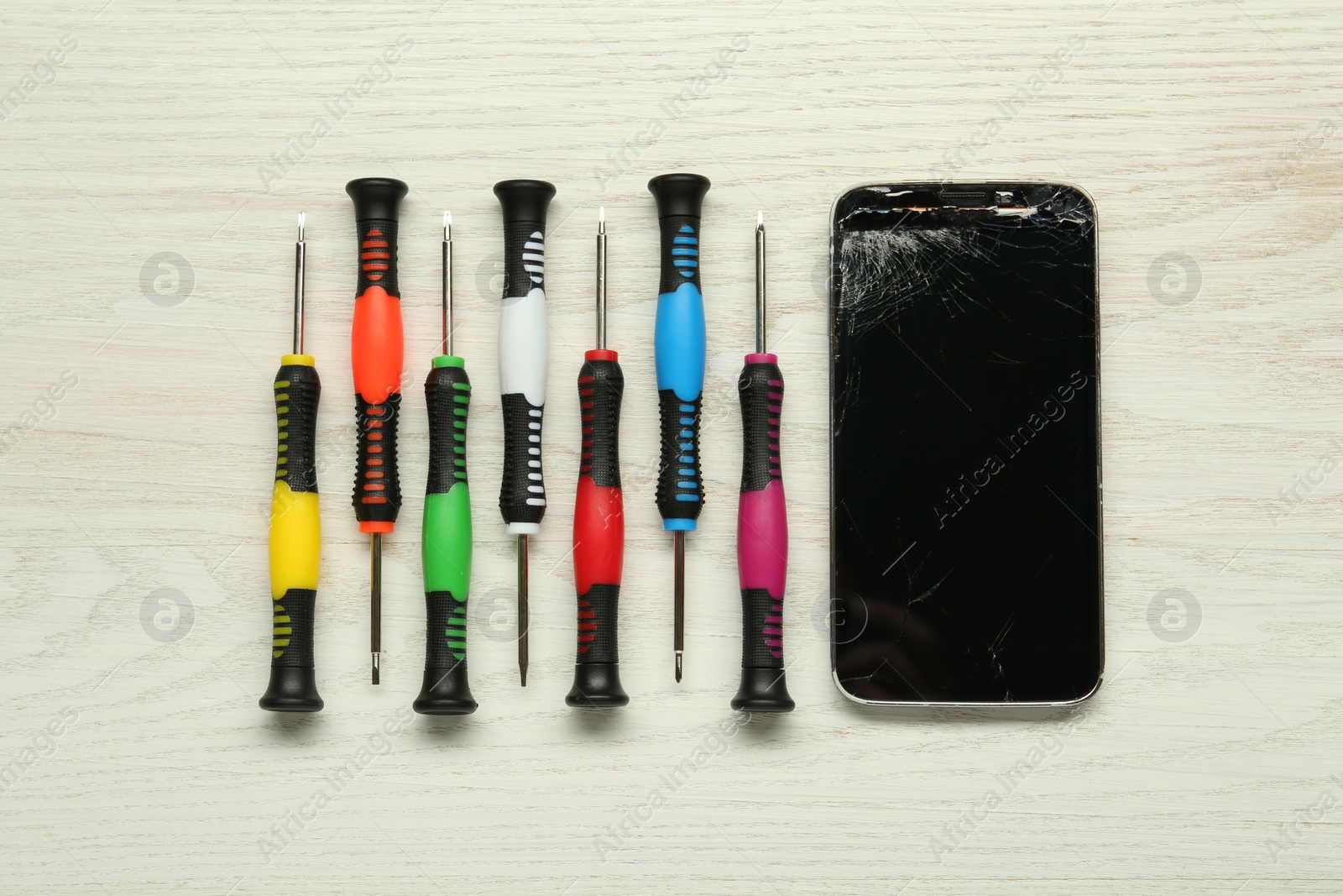 Photo of Damaged smartphone and repair tools on wooden background, flat lay