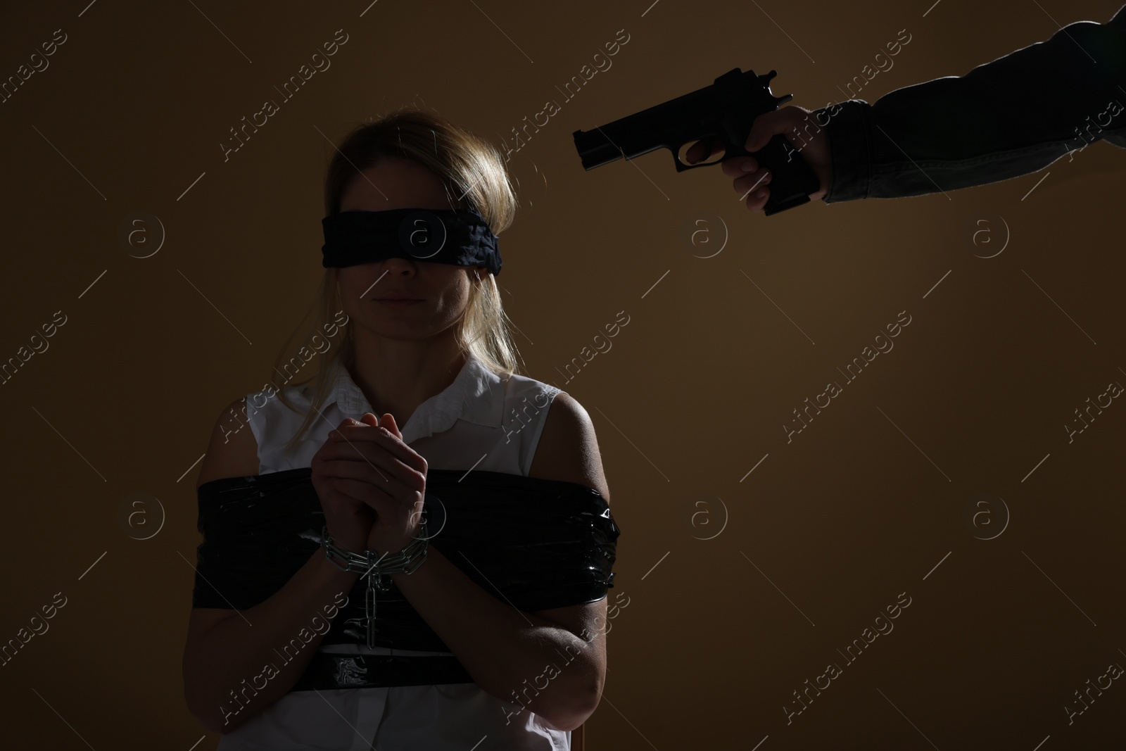 Photo of Kidnapper pointing gun at taped up and blindfolded woman taken as hostage on dark background