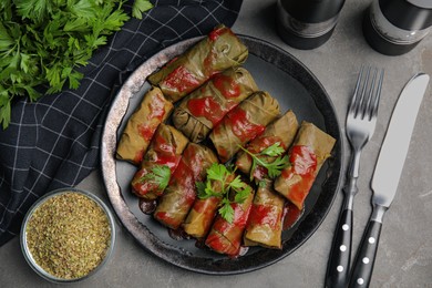 Photo of Delicious stuffed grape leaves with tomato sauce on grey table, flat lay