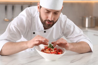 Professional chef decorating delicious spaghetti with parsley at marble table