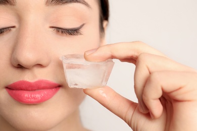 Photo of Young woman with ice cube on light background. Skin care