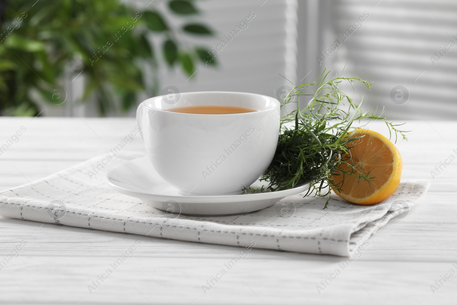 Photo of Aromatic herbal tea, fresh tarragon sprigs and lemon on white wooden table