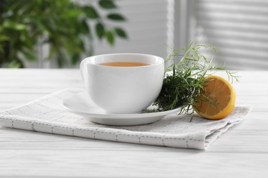 Photo of Aromatic herbal tea, fresh tarragon sprigs and lemon on white wooden table