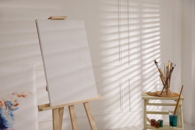 Photo of Wooden easel with empty canvas and brushes in art studio