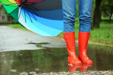 Photo of Woman with umbrella and rubber boots in puddle, closeup. Rainy weather