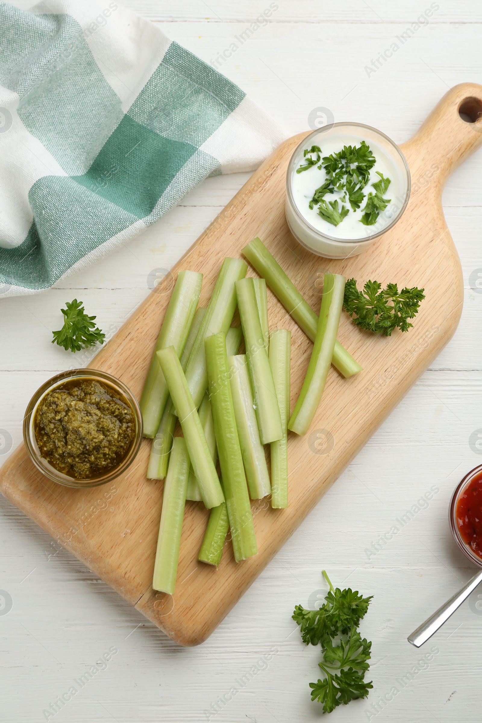 Photo of Celery sticks with different sauces and greenery on white wooden table, top view