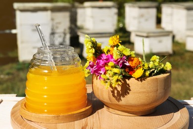 Delicious fresh honey and beautiful flowers on wooden board in apiary