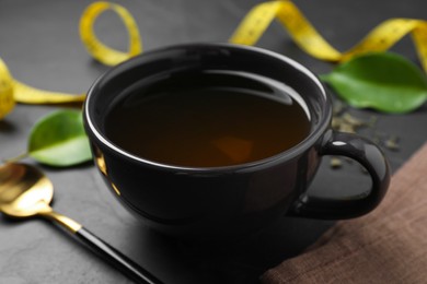 Photo of Cup of herbal diet tea on black table, closeup. Weight loss concept