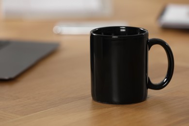 Photo of Black ceramic mug on wooden table at workplace. Space for text