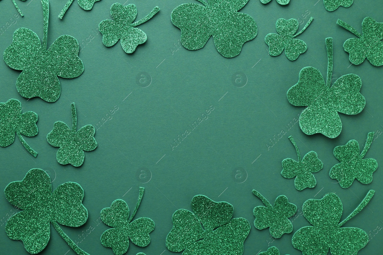 Photo of St. Patrick's day. Frame of shiny decorative clover leaves on green background, flat lay. Space for text