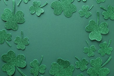 St. Patrick's day. Frame of shiny decorative clover leaves on green background, flat lay. Space for text